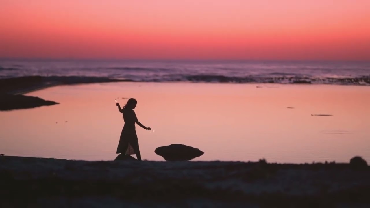 A silhouetted figure walking beside the sea at sunset